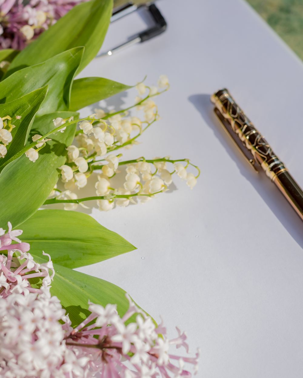 Stimmungsbild: goldener Stift neben Fliederblüten und Maiglöckchen auf Papier