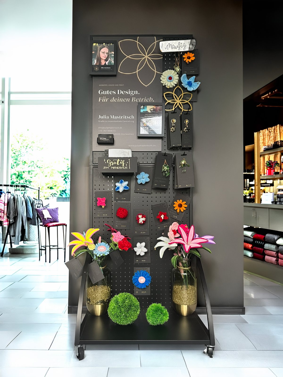 Das komplette Display: schwarze Lochwand auf Rollwagen mit Blumen, Anhängern, Hängepflanzen und Werbetafel